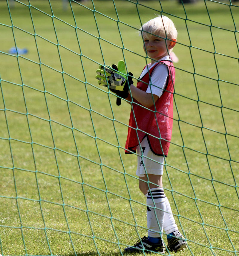 Kind steht im Tor mit Torwardhandschuhe und schaut nach hinten durch das Netz